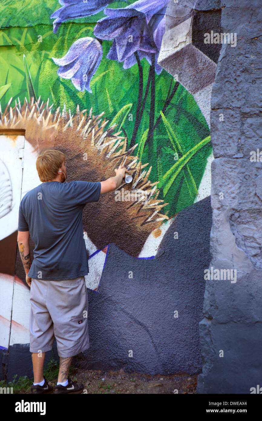 Artist working on a huge mural brightening up a dull building which backs onto a car park in Ingram Street, Glasgow, Scotland Stock Photo