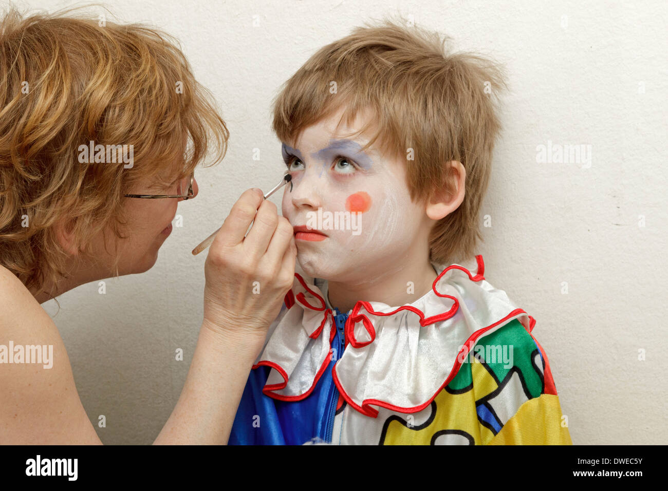 young boy dressed up as a clown getting his face painted by his mother Stock Photo