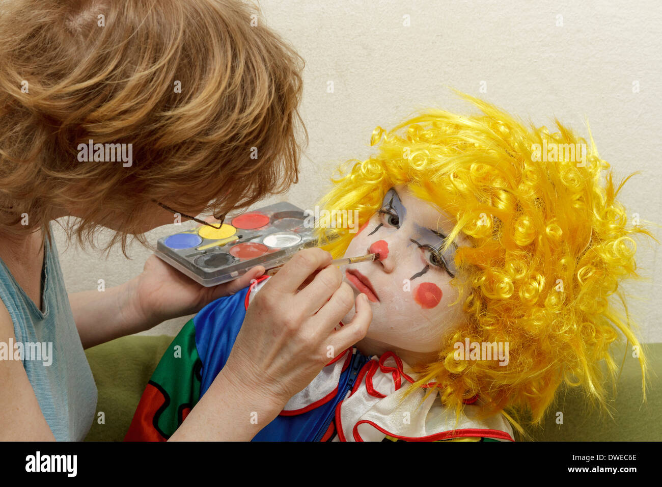 young boy dressed up as a clown getting his face painted by his mother Stock Photo