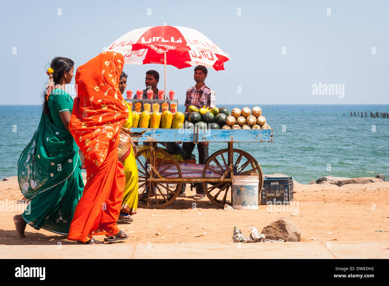 India Tamil Nadu Pondicherry Puducherry beach sand scene pretty young ladies women girls females vendor cart parasol umbrella fresh fruit papaya melon Stock Photo