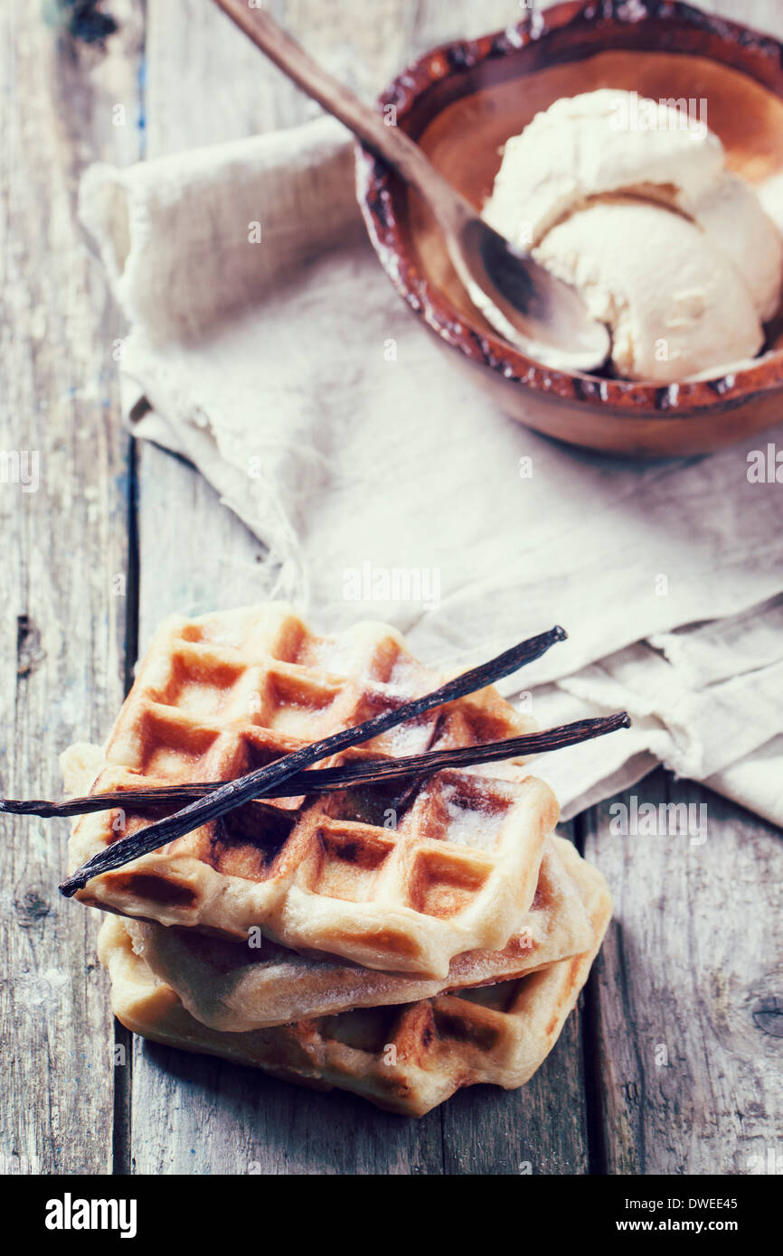White plate with fresh belgian waffles, served with ice cream and vanilla sticks over wooden table Stock Photo