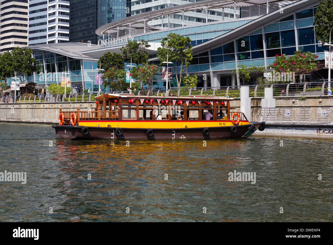 Colorful river cruise boat in Singapore next to a bridge. This is daytime and these cruises are more popular in the night. Stock Photo