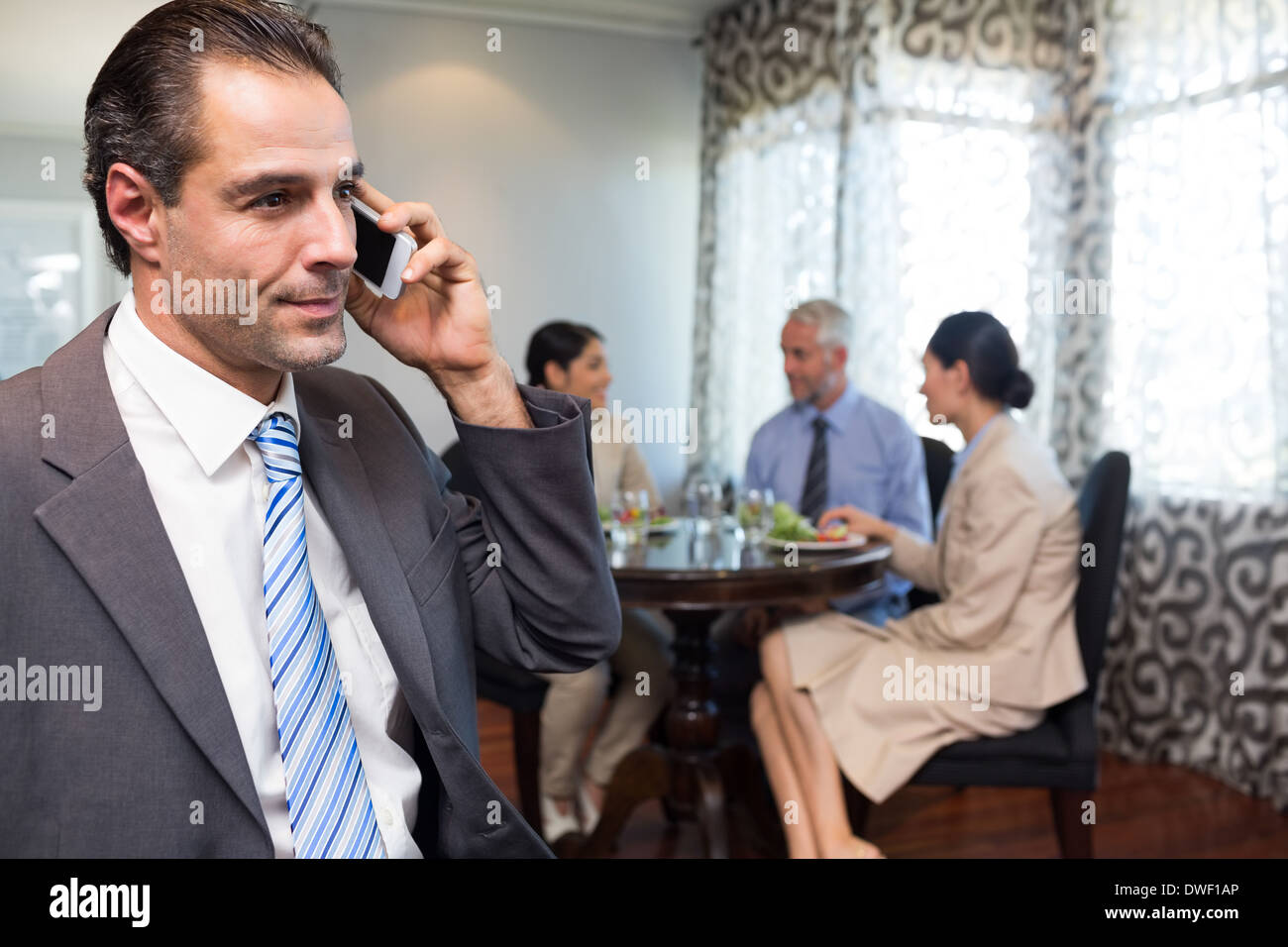 Businessman using cellphone with colleagues having meal Stock Photo