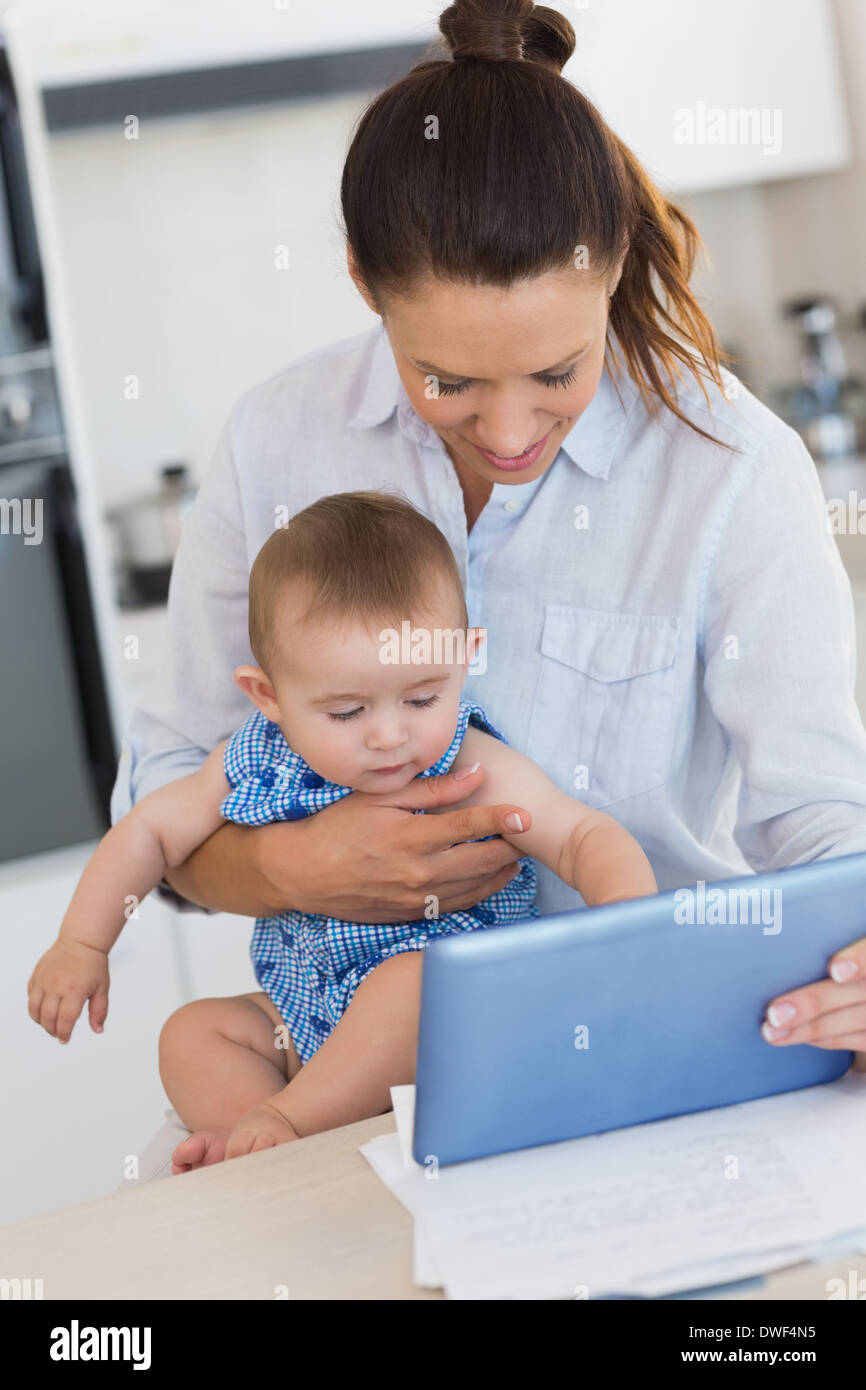 Mother calculating finances while holding baby at counter Stock Photo
