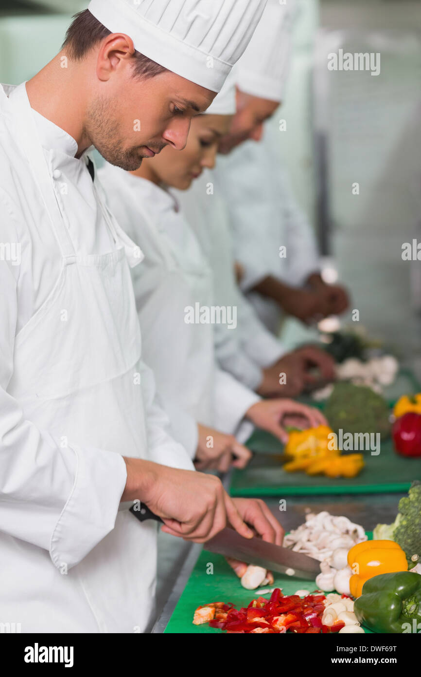 Row of trainee chefs slicing vegetables Stock Photo