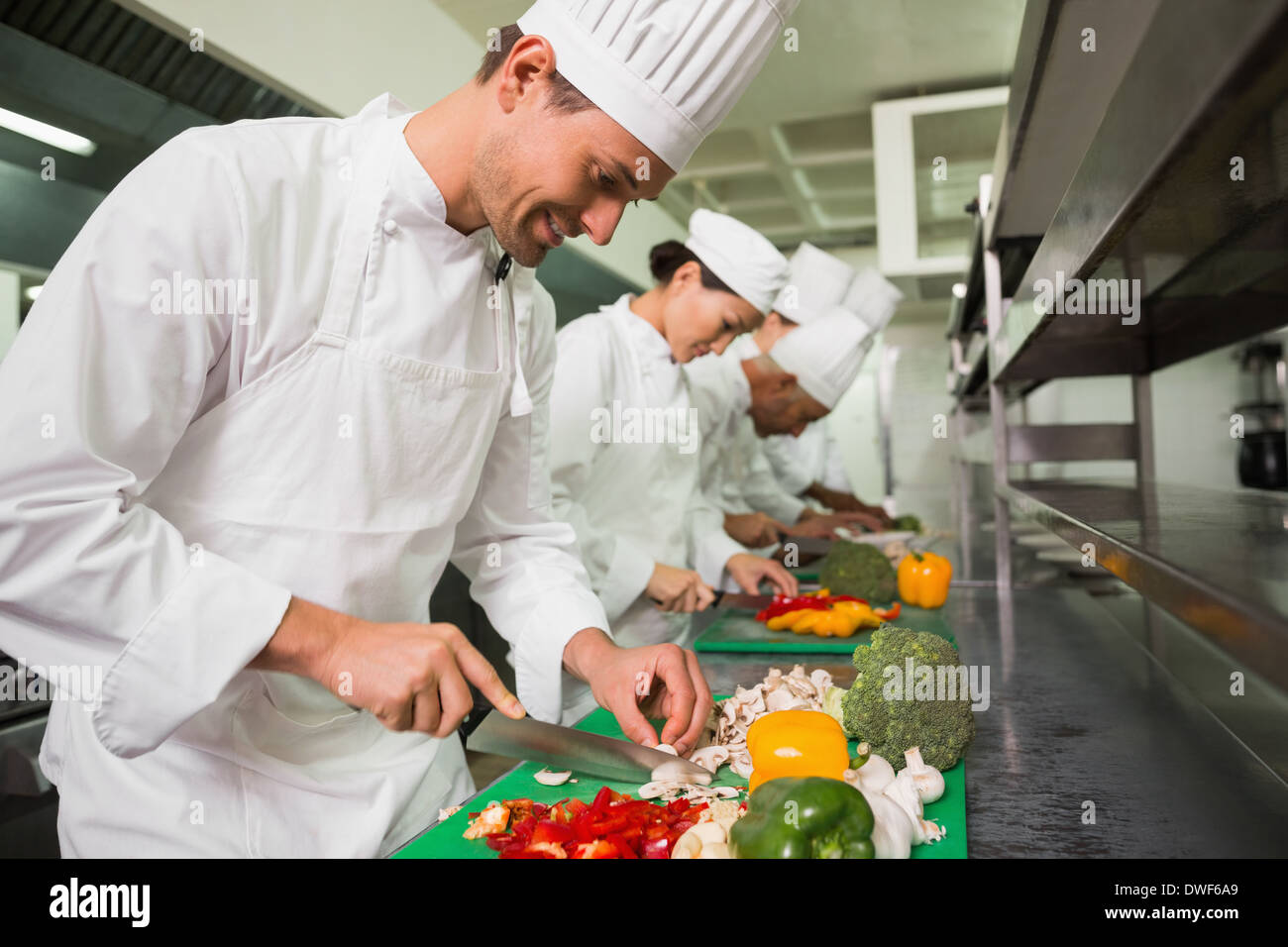 Row of trainee chefs slicing vegetables Stock Photo