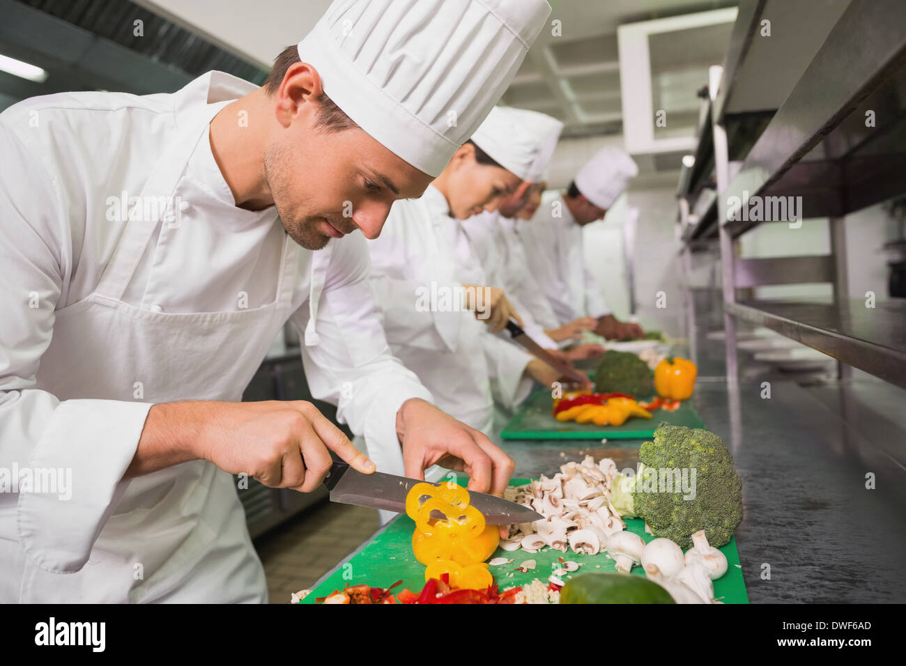 Row of trainee chefs slicing vegetables Stock Photo