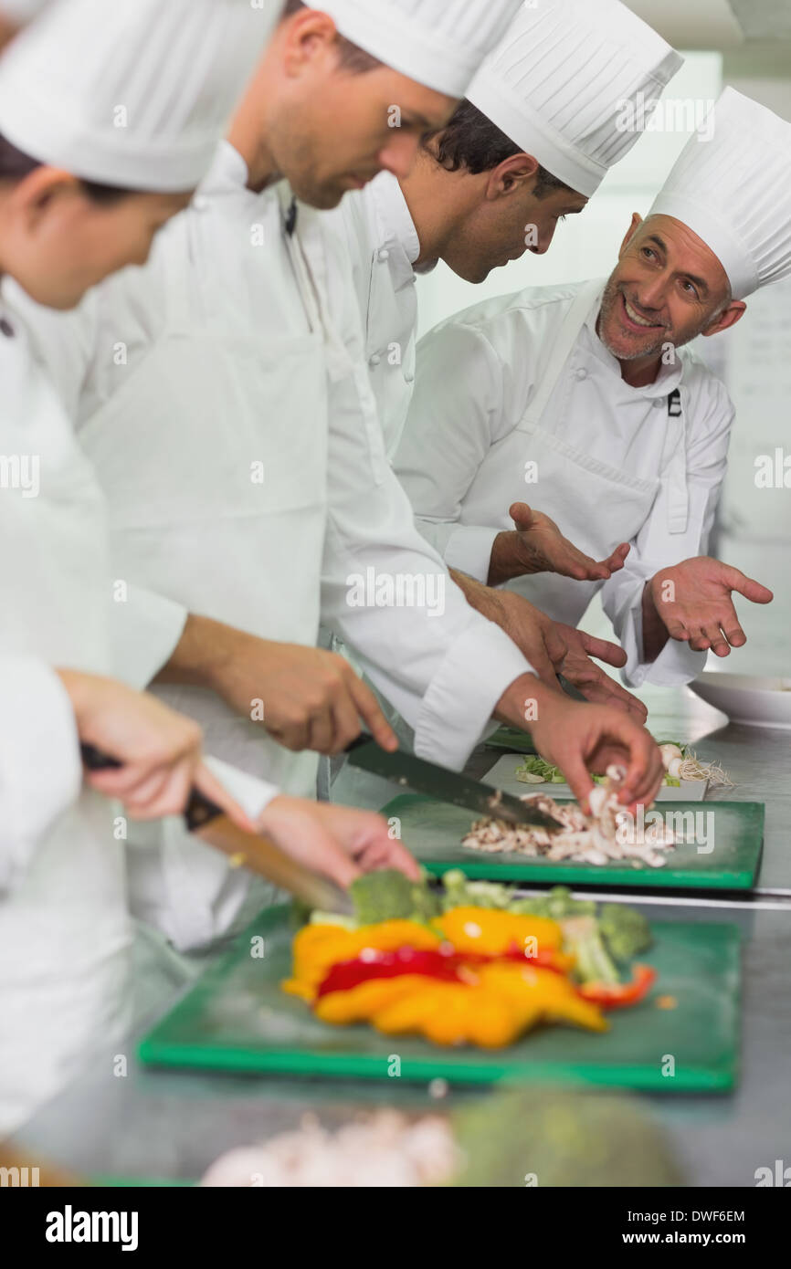 Row of trainee chefs slicing vegetables with tutor watching Stock Photo