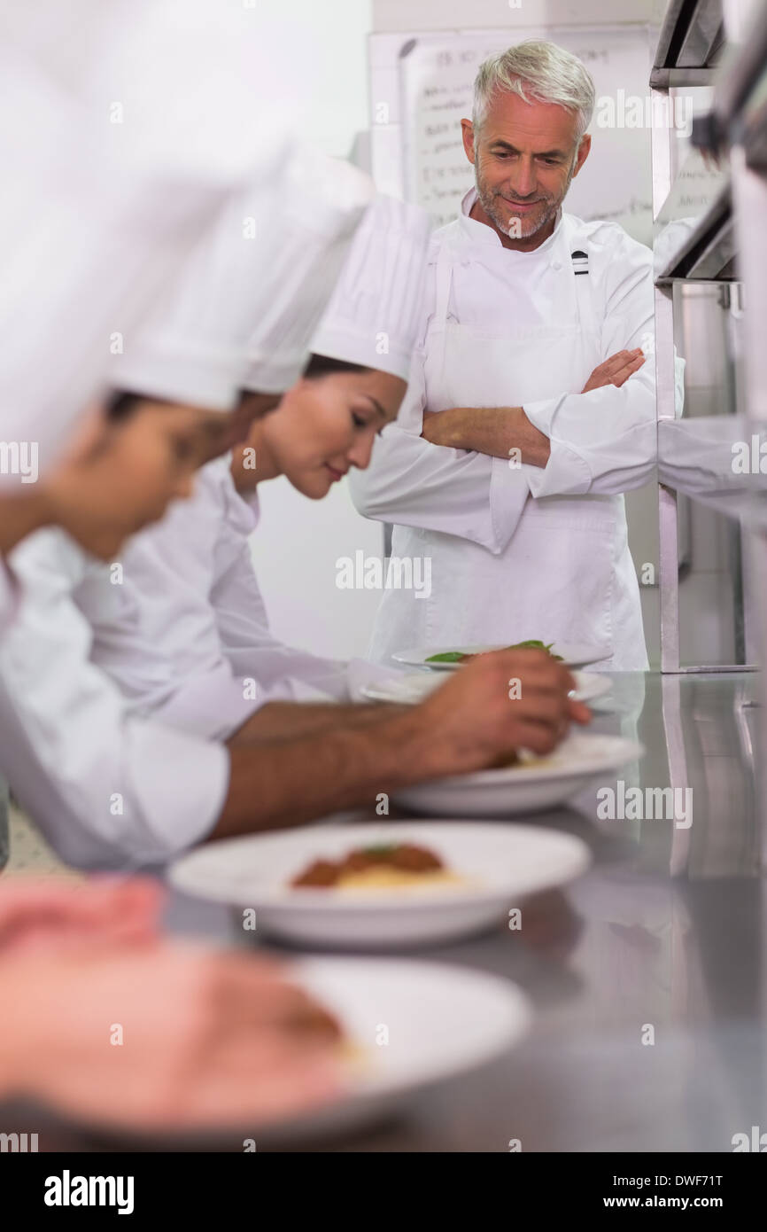 Head chef watching row of chefs garnishing spaghetti dishes with basil