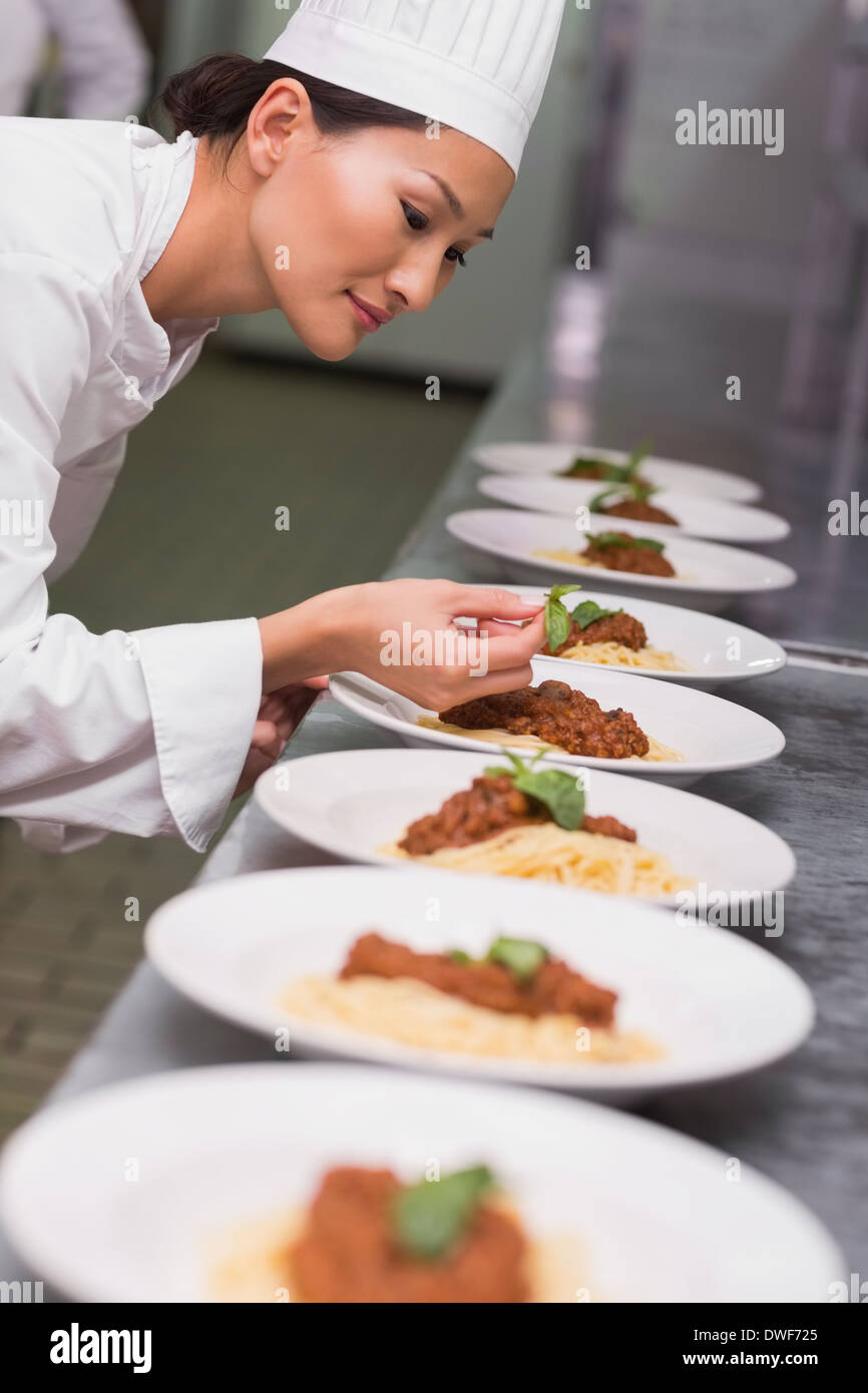 Happy chef putting basil leaf on spaghetti dish Stock Photo