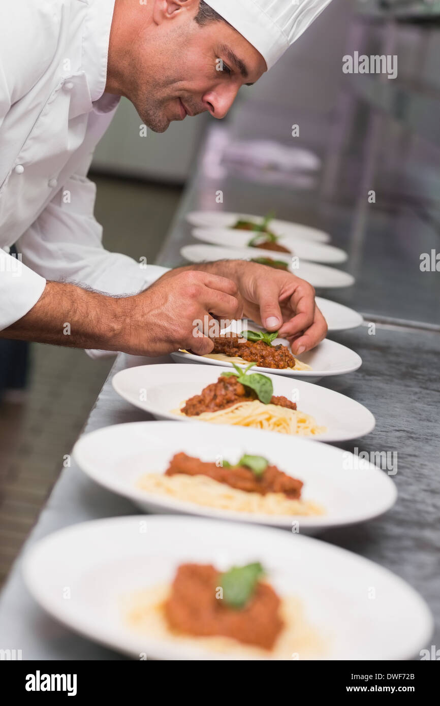 Happy chef putting basil leaf on spaghetti dish Stock Photo