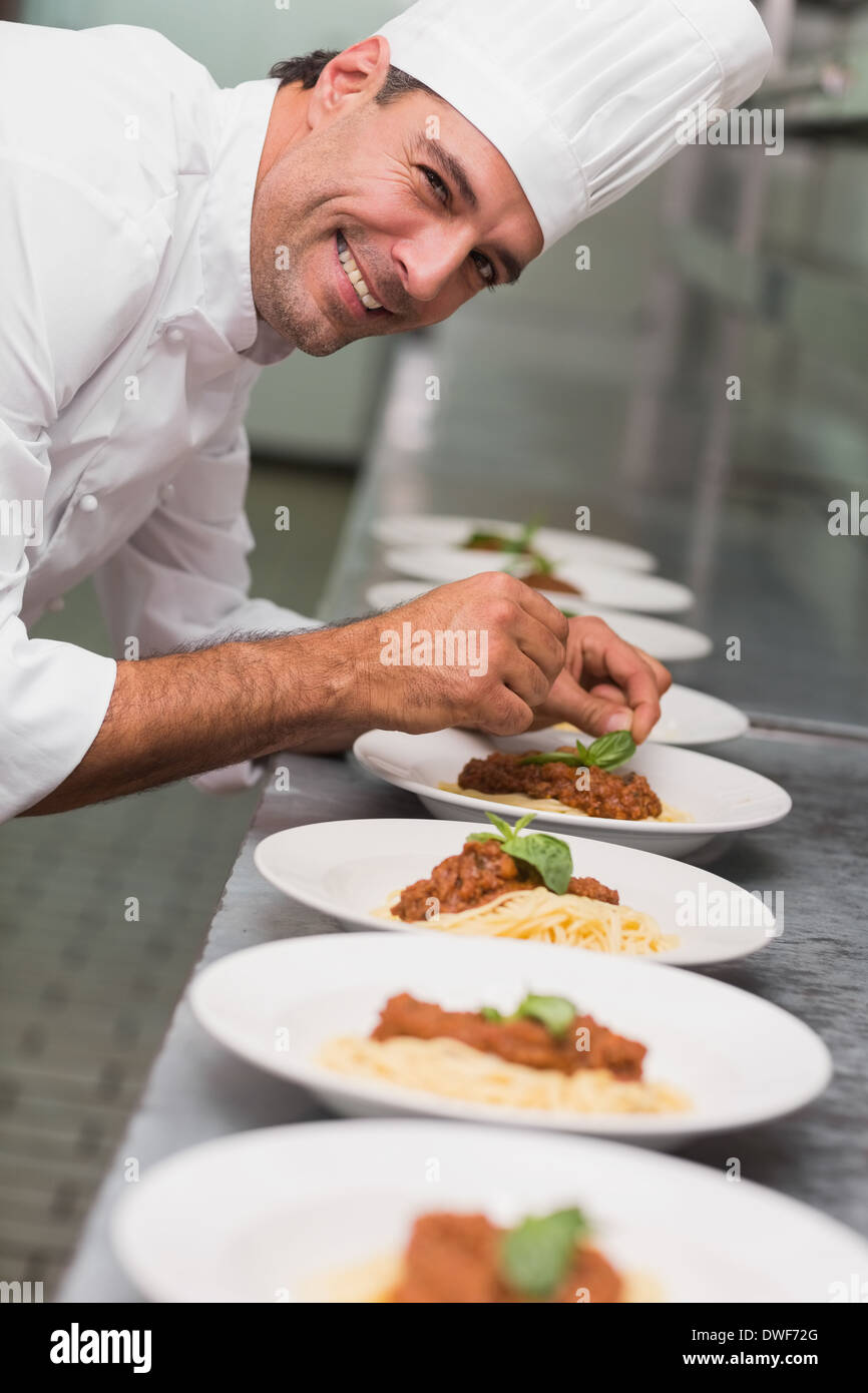 Happy chef putting basil leaf on spaghetti dish Stock Photo