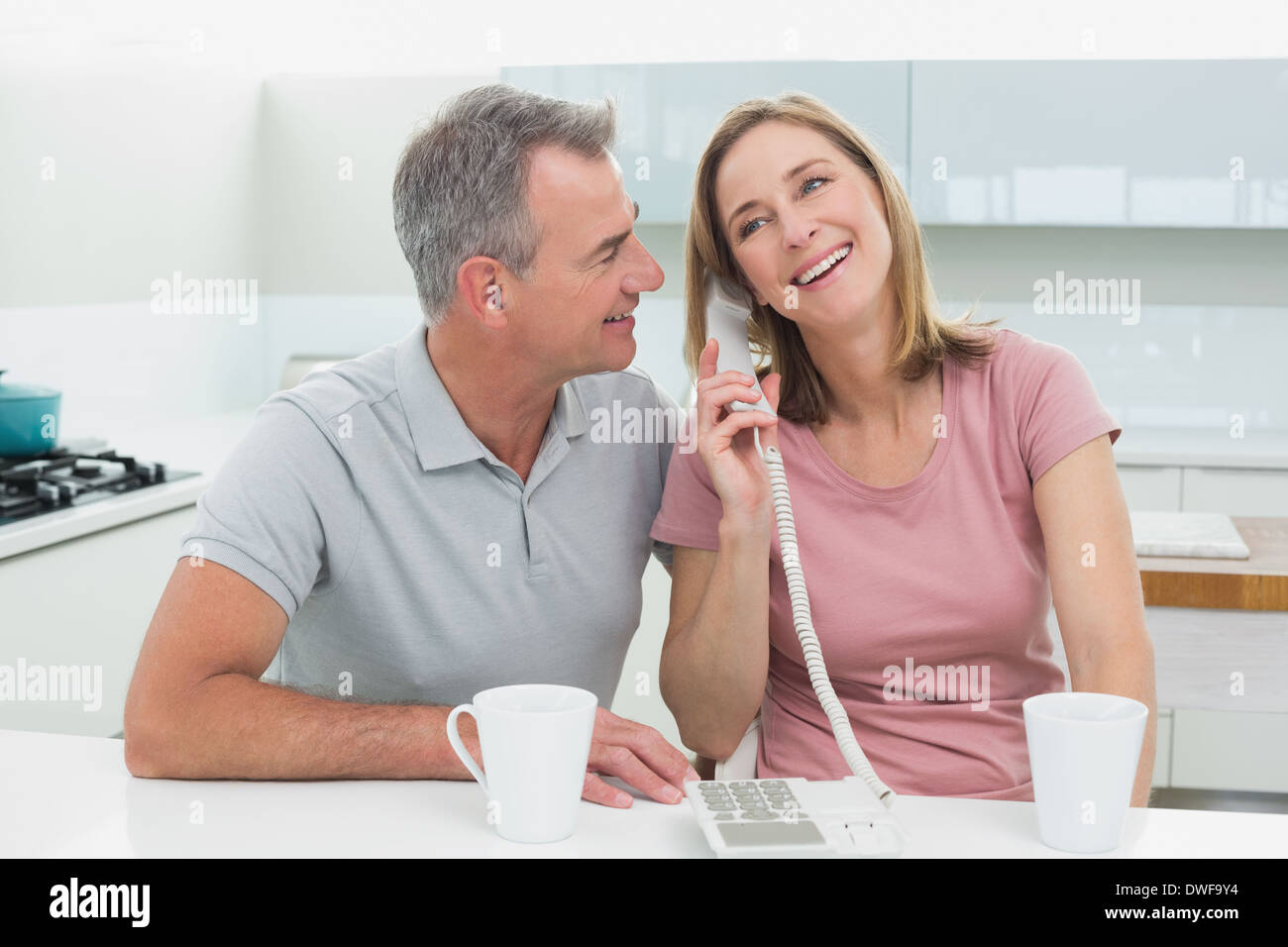 Happy couple using landline phone in kitchen Stock Photo