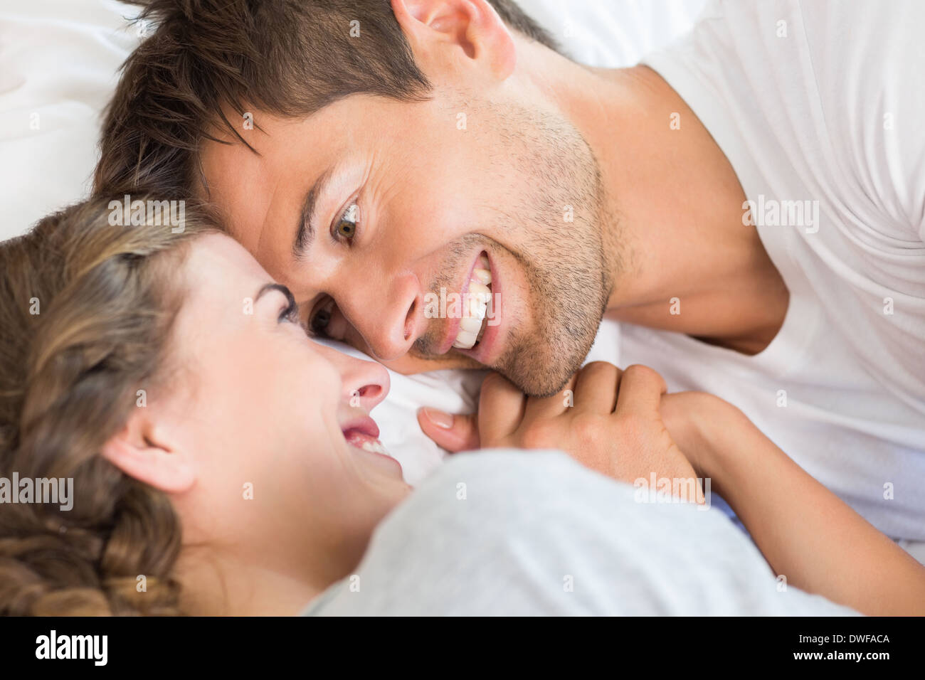 Happy couple lying on bed holding hands Stock Photo