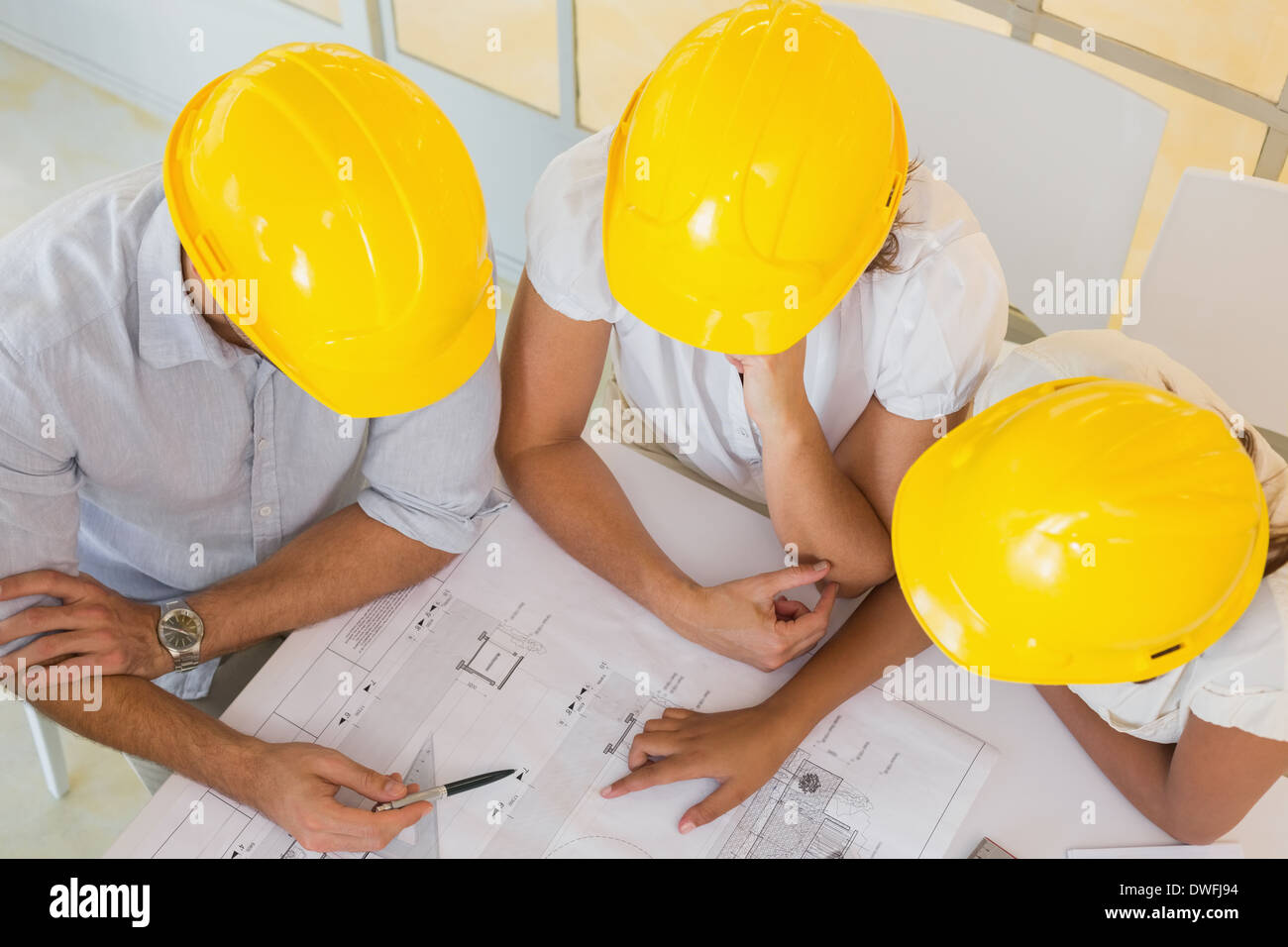 Architects in yellow helmets working on blueprints at office Stock Photo
