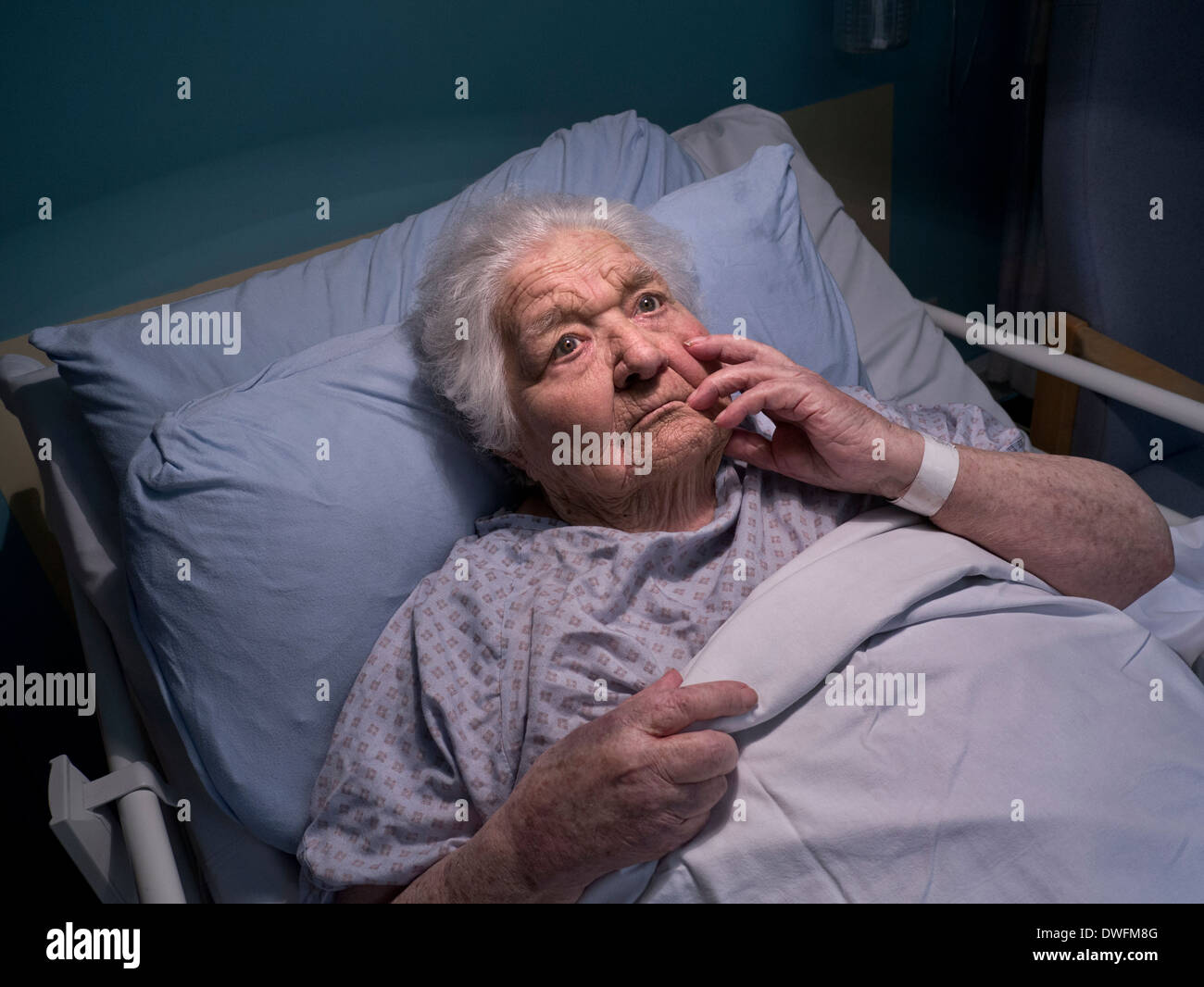 ELDERLY LADY MEMORY CARE HOSPITAL BED PENSIVE CONFUSED DEMENTIA  Very elderly lady at 100 years of age in thought in hospital care ward bed at night Stock Photo