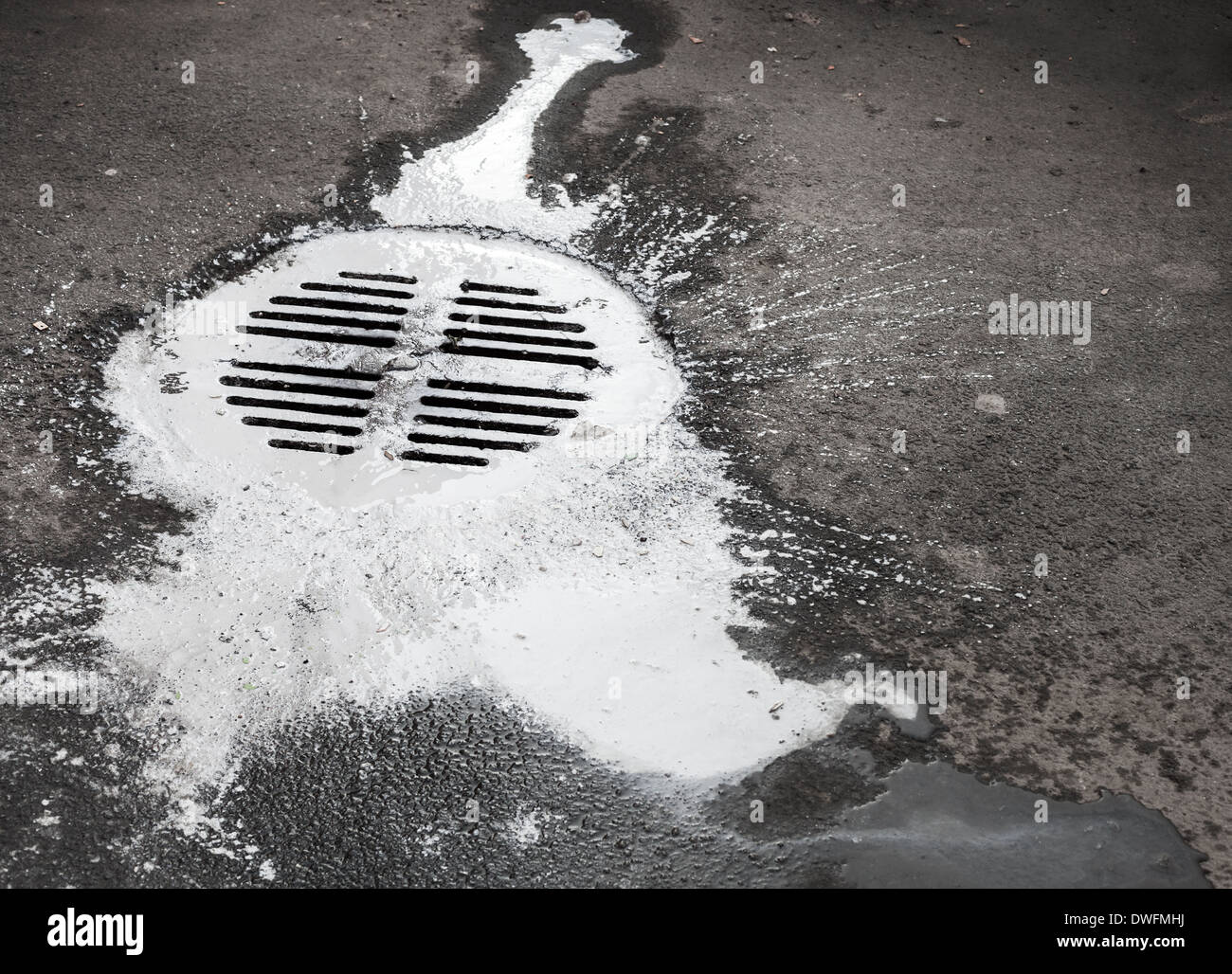 White paint flows into the manhole. Pollution metaphor Stock Photo