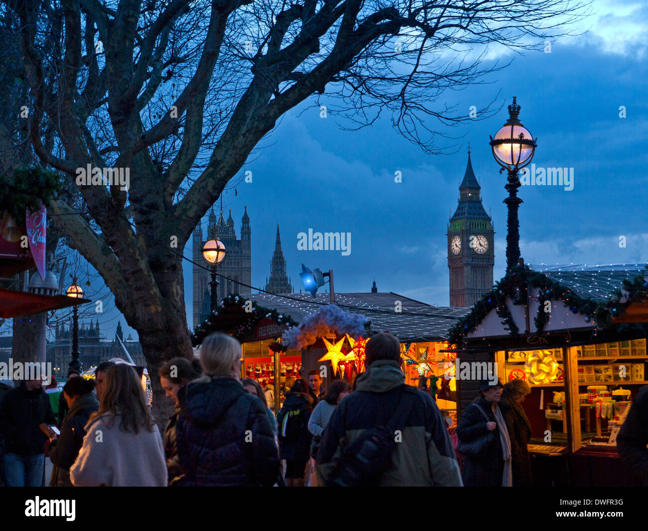 South Bank Christmas market stalls and shoppers with Houses of Parliament behind at dusk London