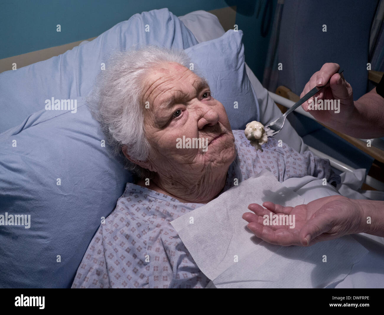 Elderly lady feeding food fed with carer attempting to feed her a meal with difficulty in hospital care bed at night Stock Photo