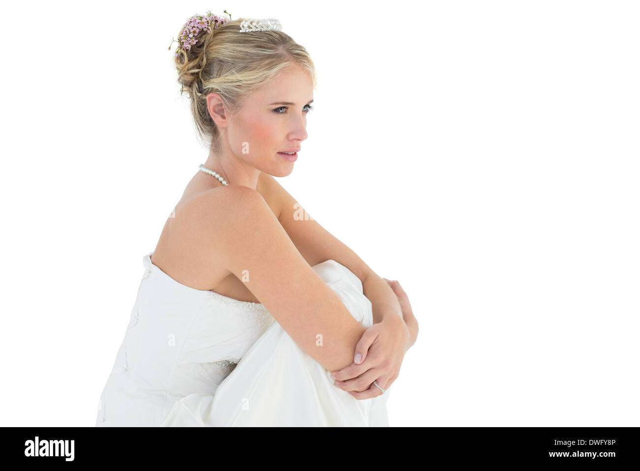 Thoughtful bride hugging knees over white background Stock Photo