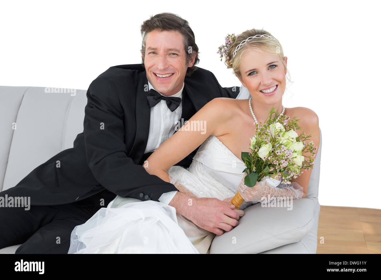 Bride and groom with flower bouquet sitting on sofa Stock Photo