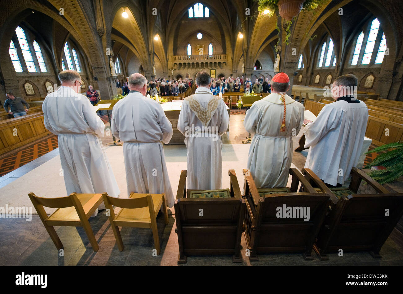 A priest, a cardinal (red cap) and their helpers are standing during a mass in the roman catholic 'Onze lieve Vrouwekerk' Stock Photo