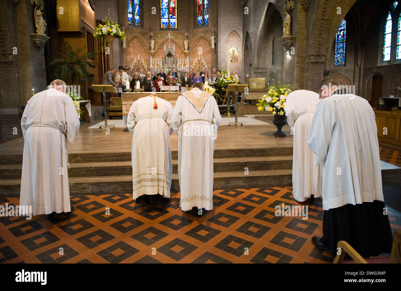 A priest, a cardinal with their helpers are bowing towards the altar at the end of a mass in the catholic church Stock Photo