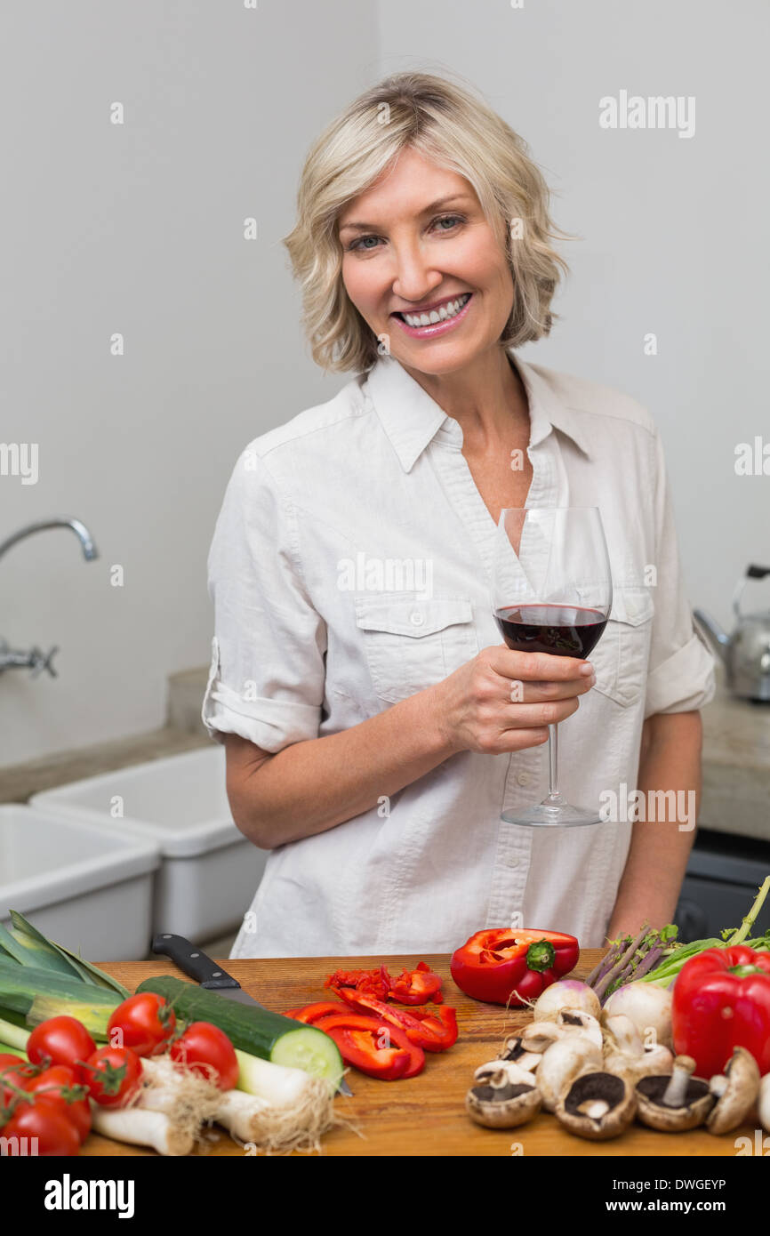 Happy mature woman with vegetables and wine glass in kitchen Stock Photo