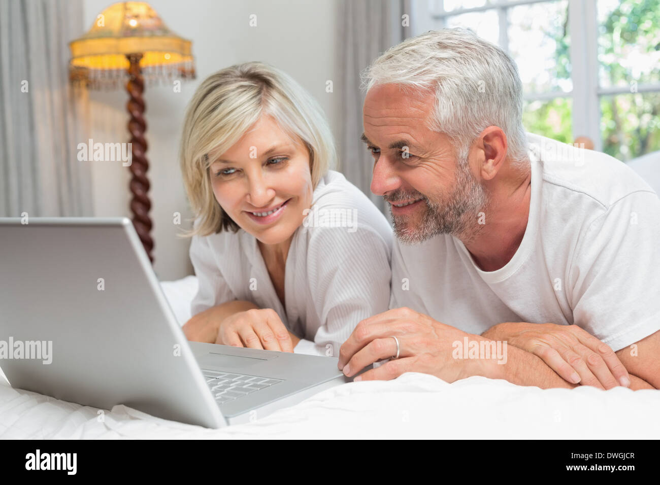 Happy mature couple using laptop in bed Stock Photo