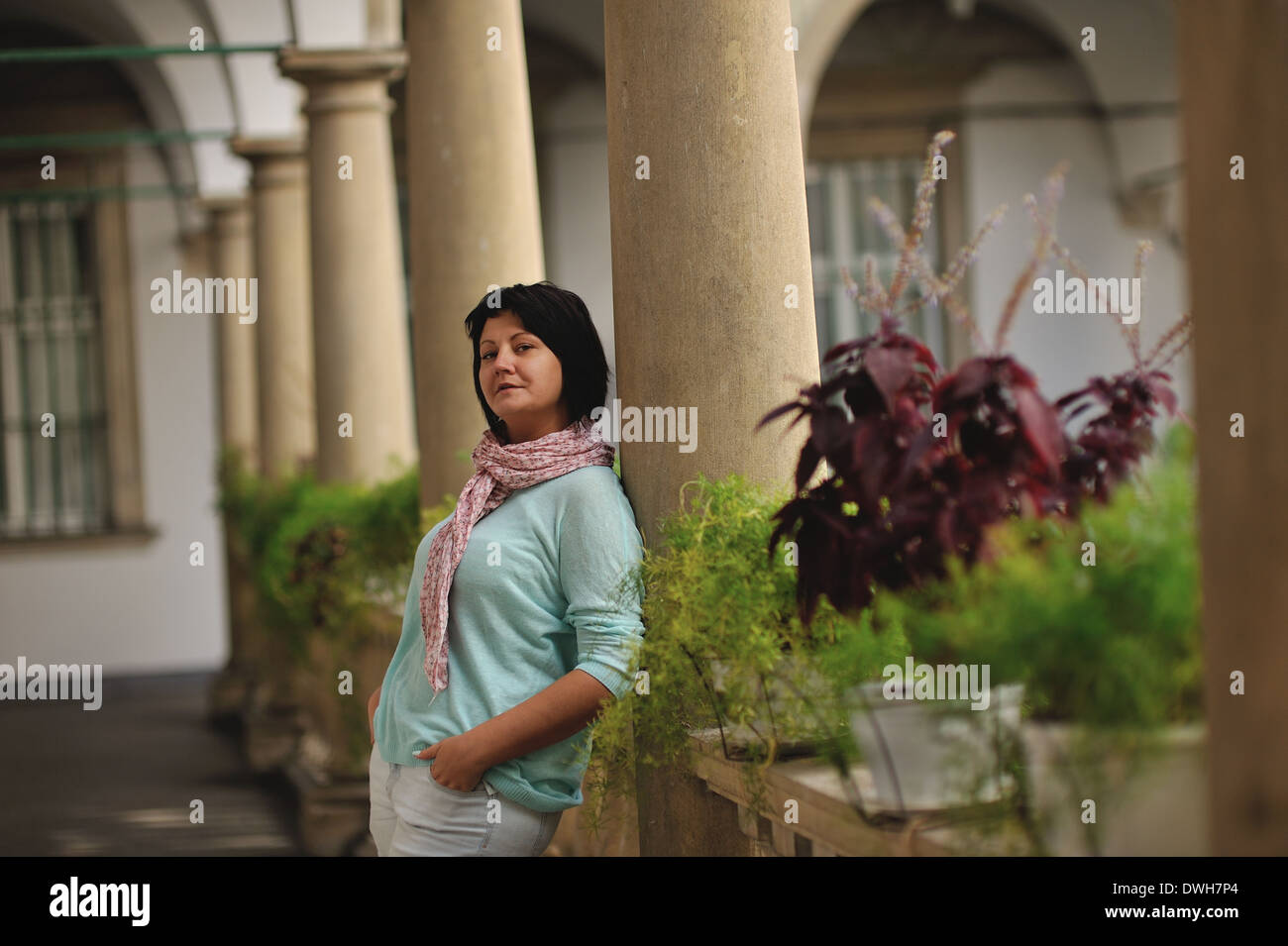 woman in trousers posing in antique balcony with stone pillars and railings Stock Photo