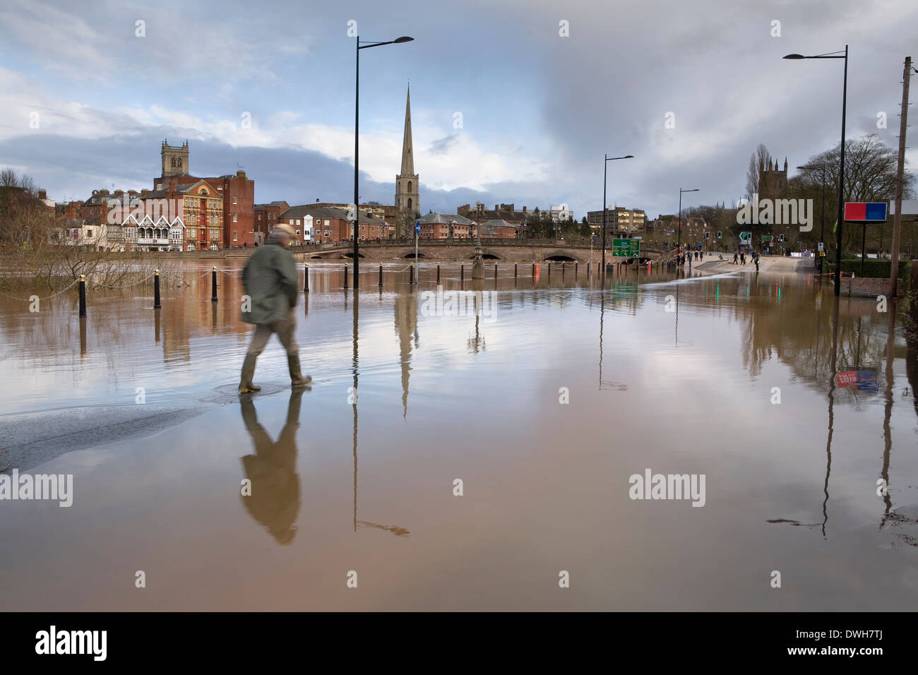 A photograph of the River Severn flooding over Tybridge Street in Worcester as a pedestrian tries to cross on foot. Stock Photo