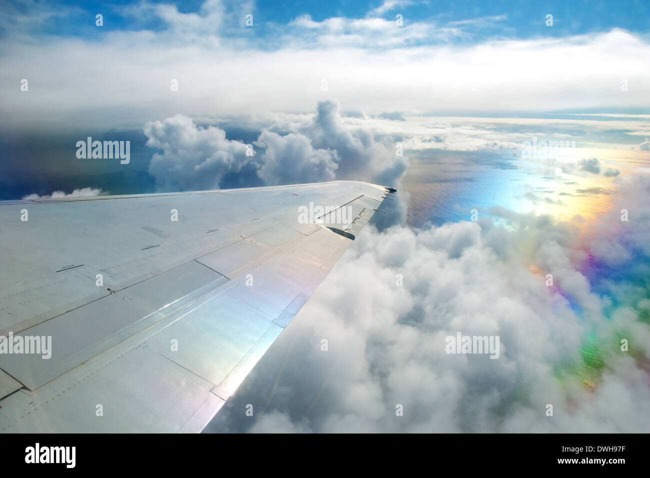 Wing of airplane flying above clouds in the sky and with a view of the ocean in background Stock Photo