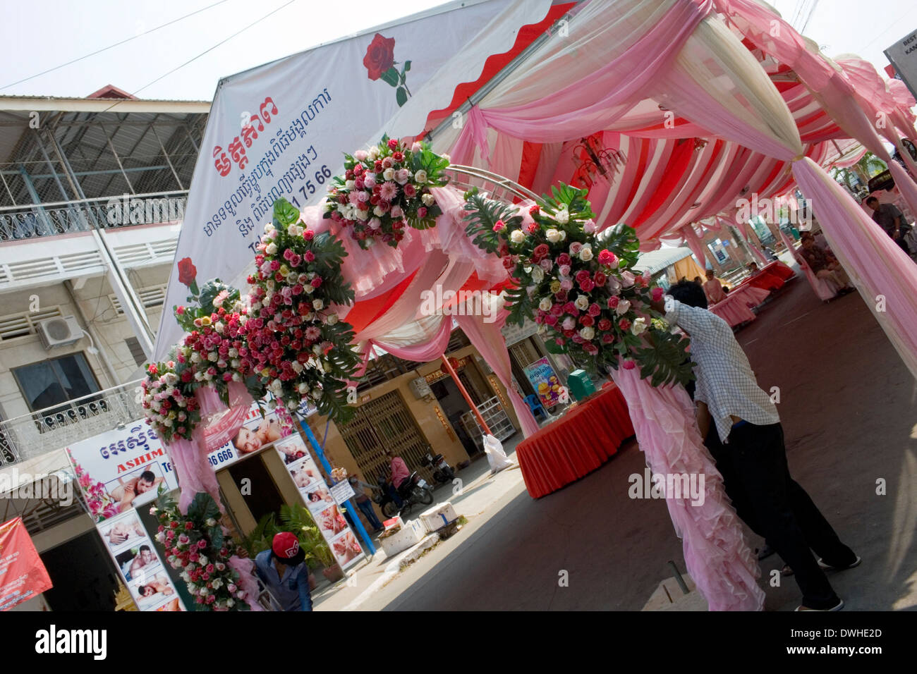 A man is hanging a synthetic rose floral arrangement on a wedding tent on a city street in Kampong Cham, Cambodia. Stock Photo