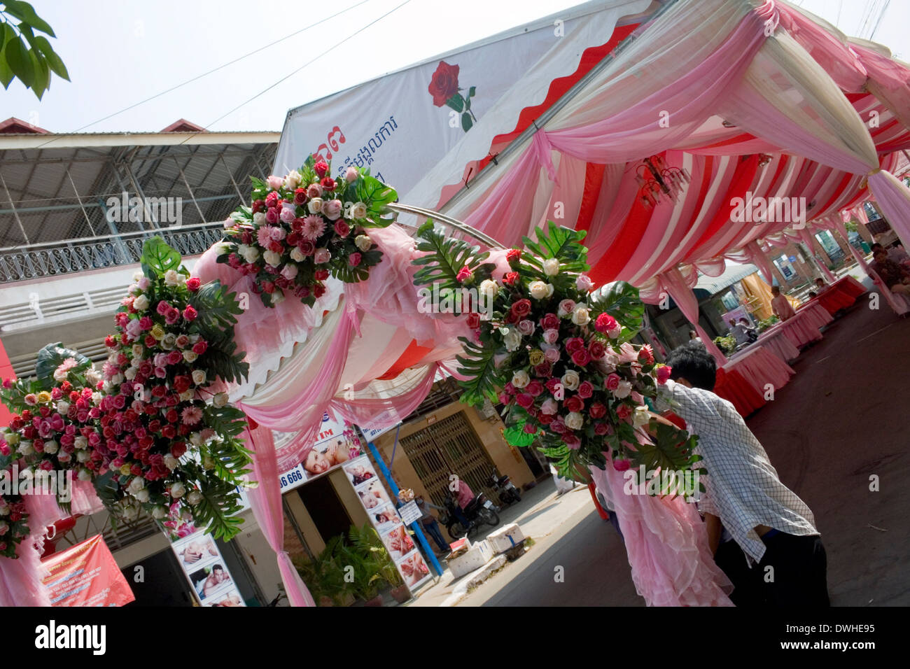 A man is hanging a synthetic rose floral arrangement on a wedding tent on a city street in Kampong Cham, Cambodia. Stock Photo