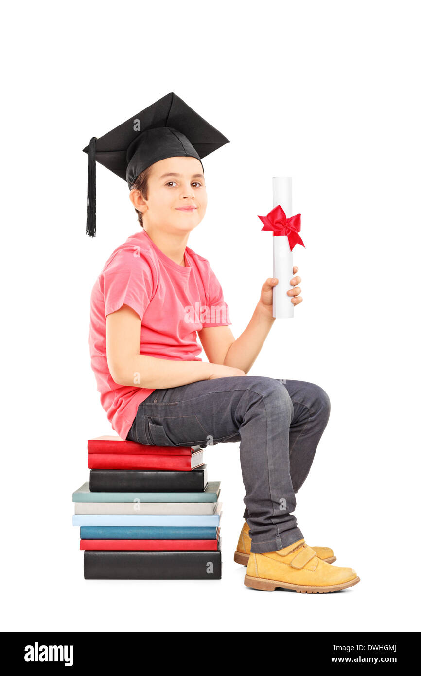 Boy with graduation hat sitting on stack of books and holding a diploma Stock Photo