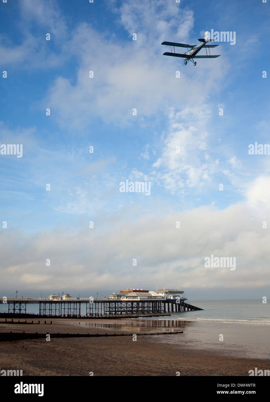 Old biplane flying over the pier and beach at Cromer on the Norfolk coast in southeast England Stock Photo