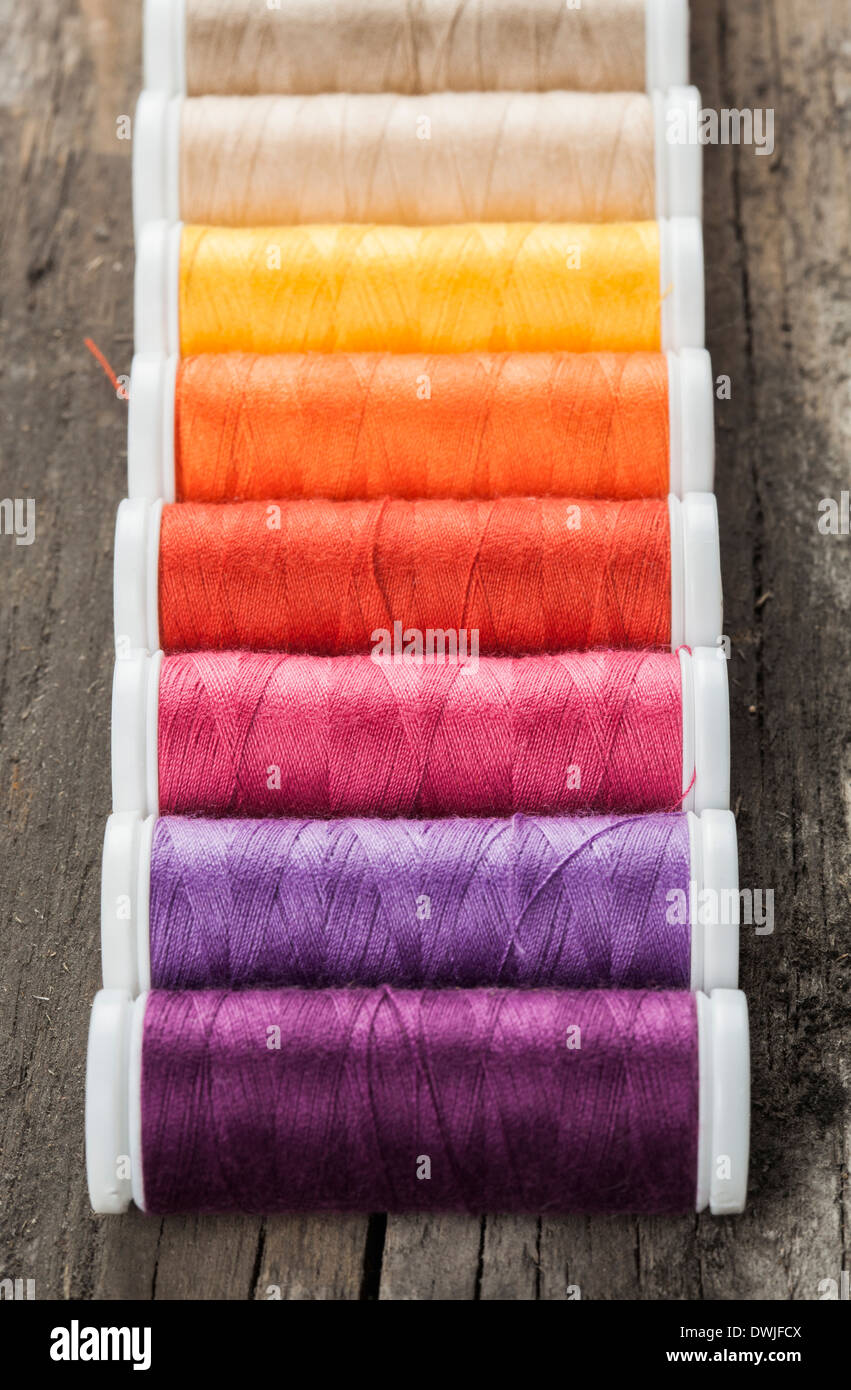 Single row made of color spools of sewing threads, on wooden background Stock Photo