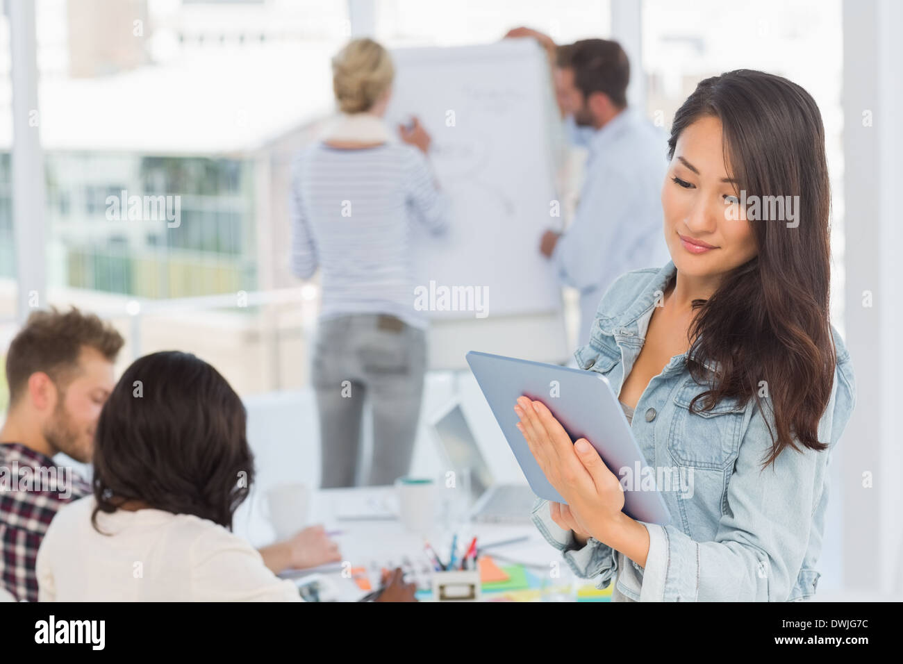 Asian woman using her tablet pc while her colleagues are working Stock Photo