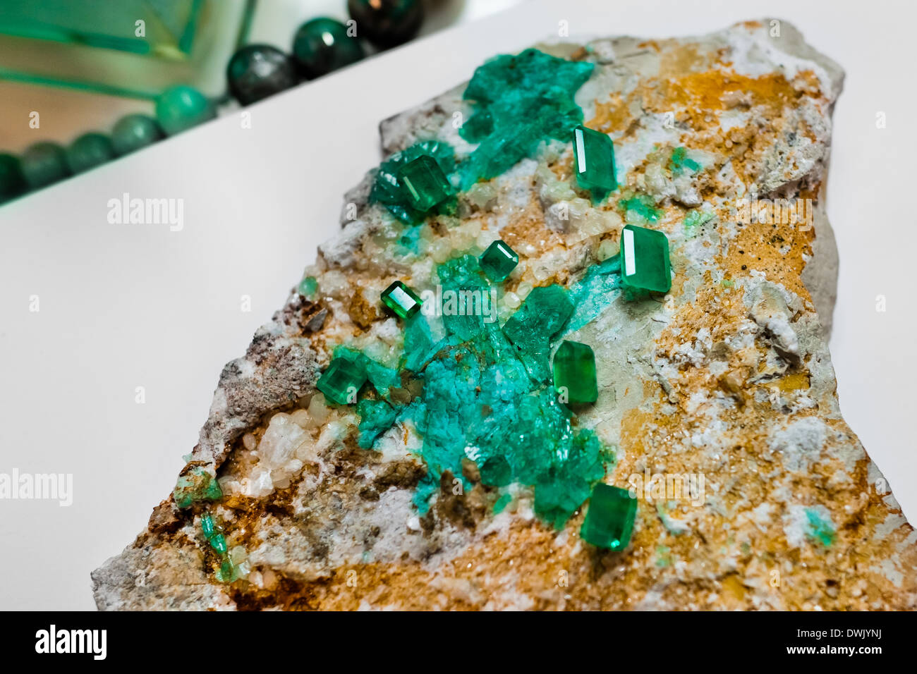 A rough emerald gemstone, together with the polished stones, are seen