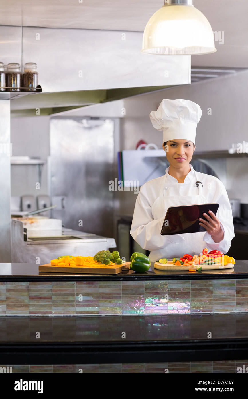 Female chef using digital tablet while cutting vegetables in kitchen Stock Photo