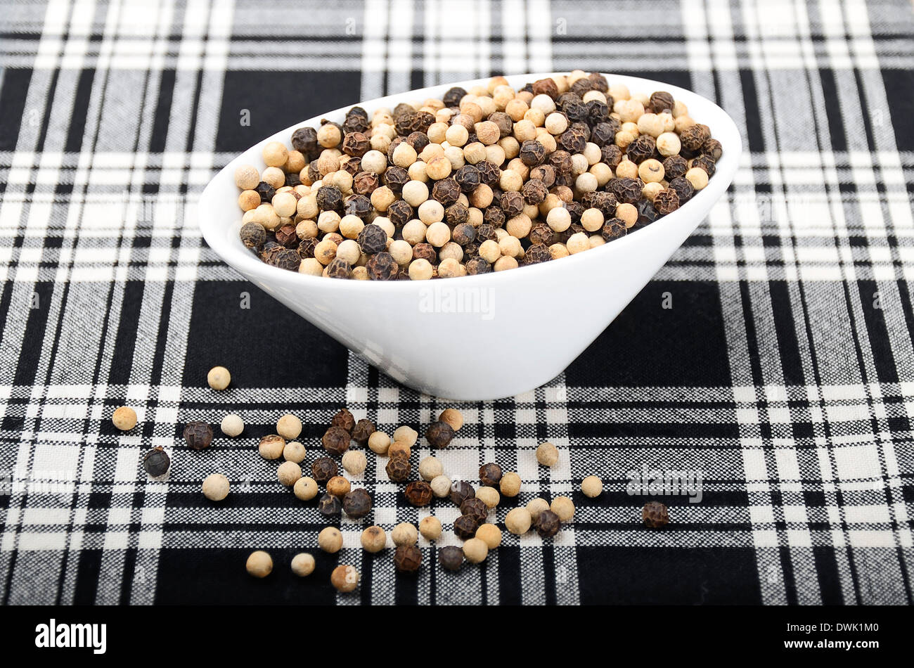 French Mignonette Pepper - White and black peppercorns in a white porcelain bowl on black and white fabric Stock Photo