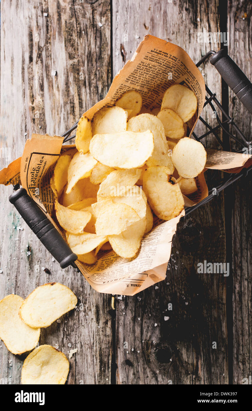 Top view on basket with potato chips with sea salt over old wooden table. Stock Photo