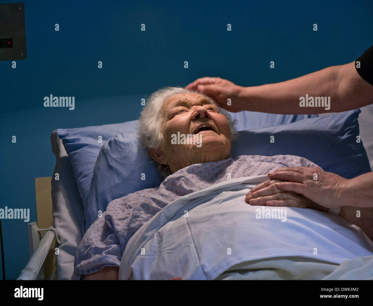 Contented smiling senior old age elderly lady in hospital bed at night with comforting hand of carer nurse Stock Photo