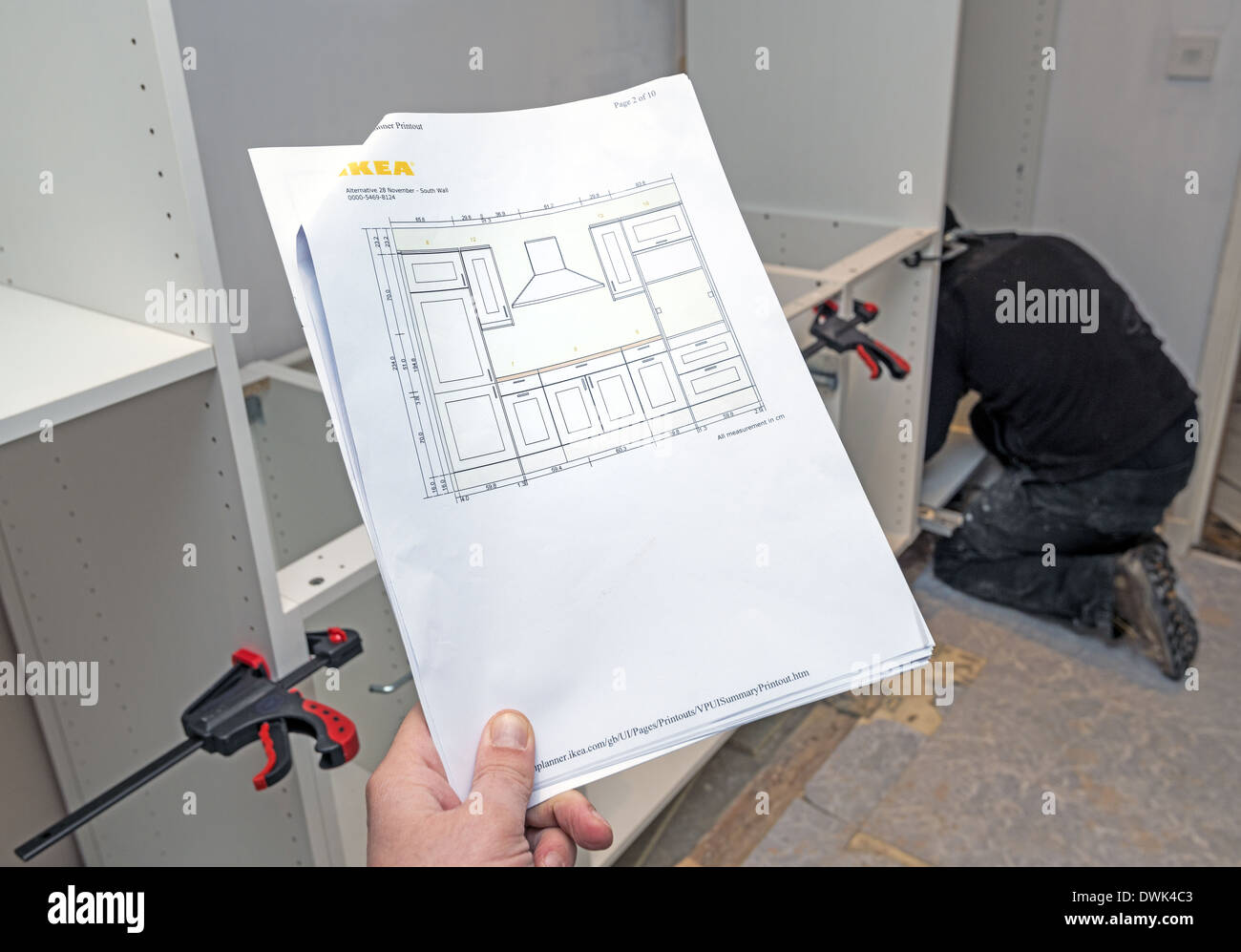 Man holding Ikea kitchen plan with worker installing kitchen in the background Stock Photo