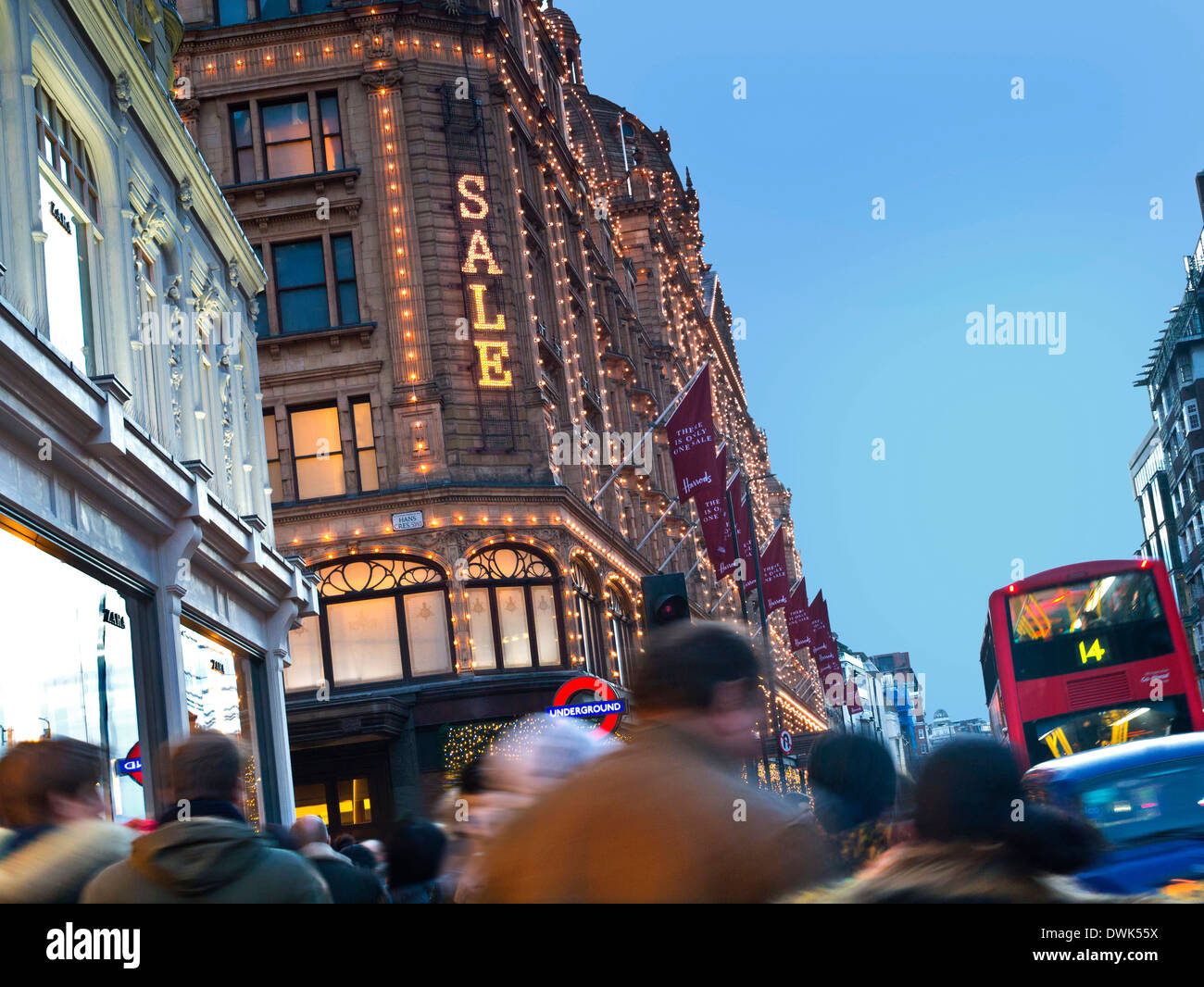 Harrods department store at dusk with lit 'Sale' sign and crowds of shoppers taxi and red bus Knightsbridge London SW1 Stock Photo