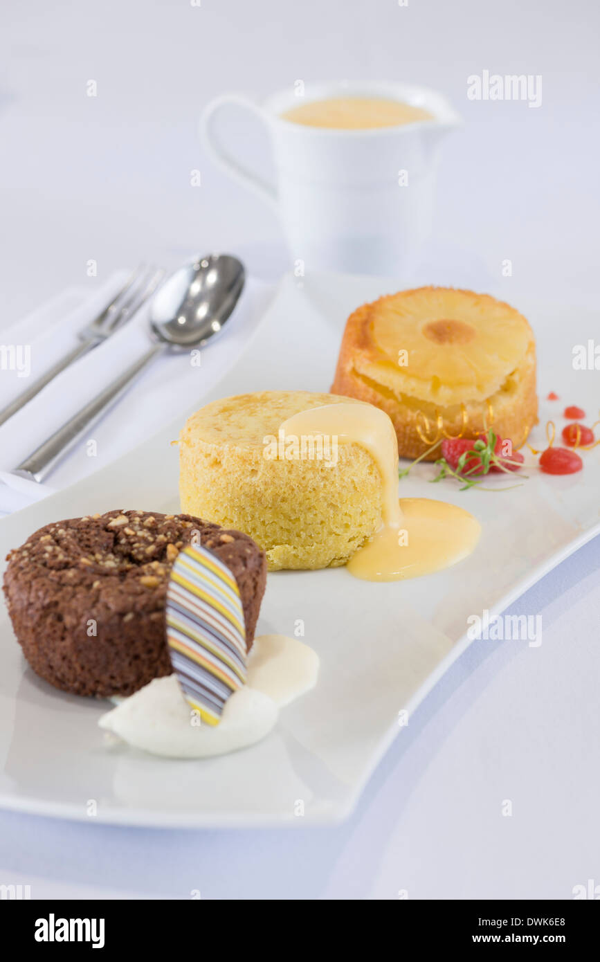 Trio of desserts, including chocolate brownie, sponge pudding and queen of puddings and custard Stock Photo