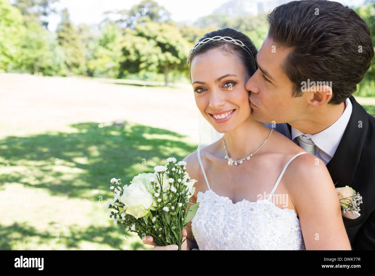 Groom kissing beautiful bride on cheek in garden Stock Photo - Alamy