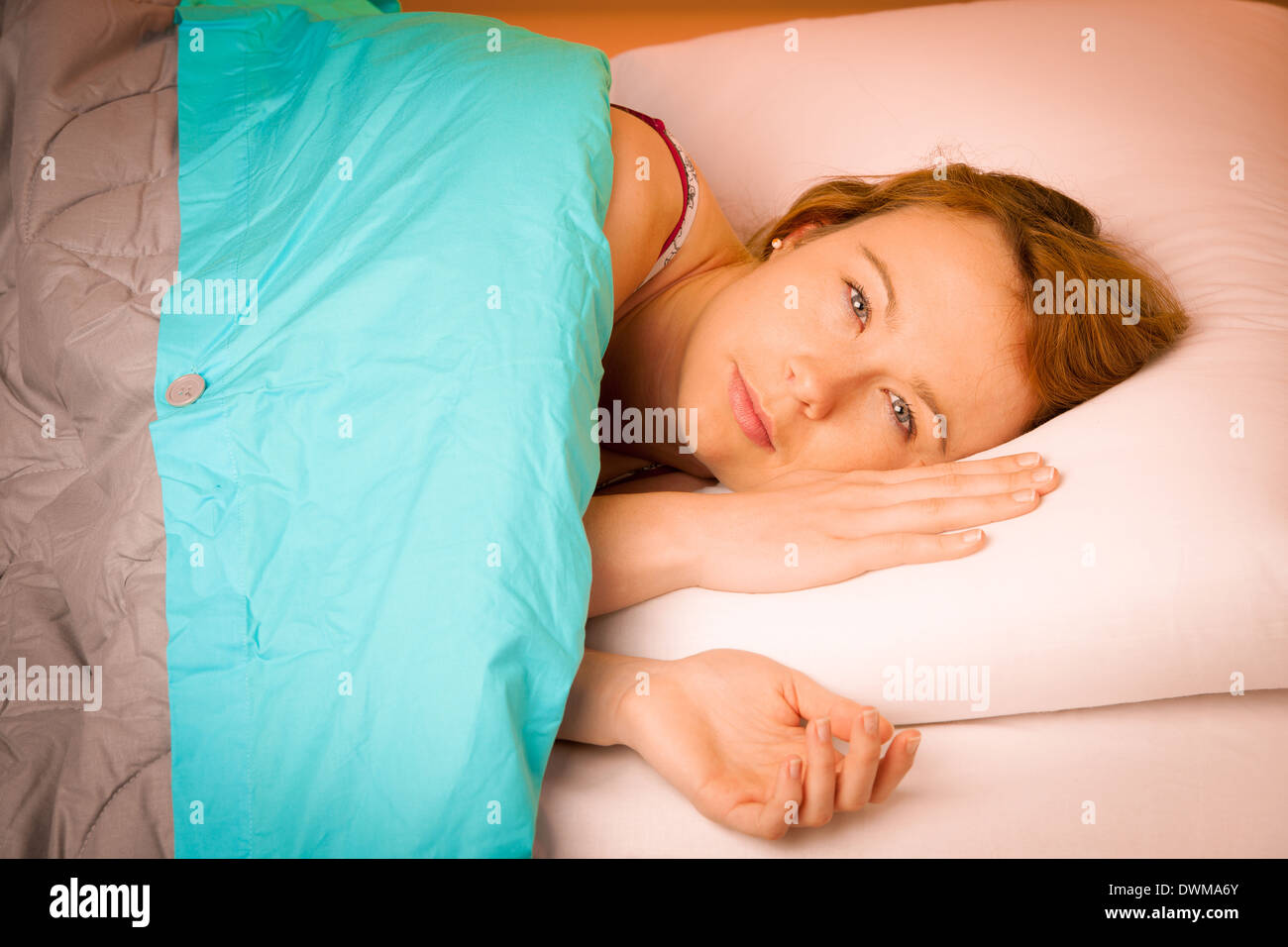 Woman lying on pillow in bed, covered with blue blanket Stock Photo