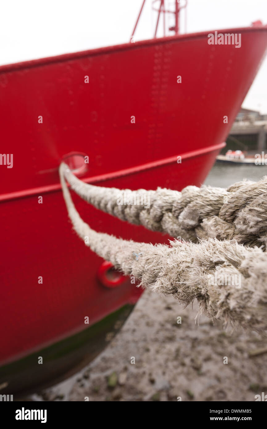 strong mooring rope as a holdfast to keep bright red steel boat hull secure on tidal jetty wharf