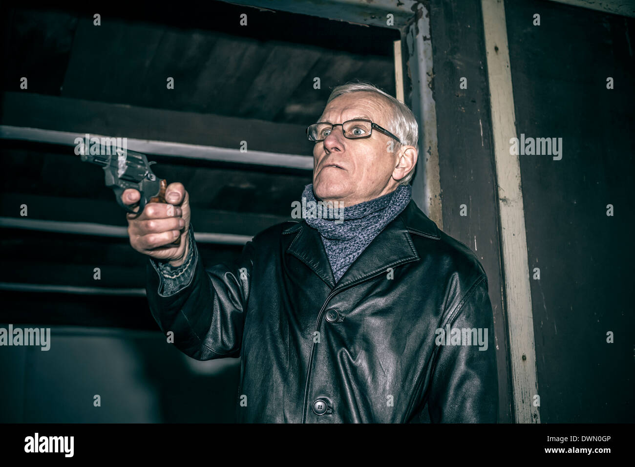 Dangerous senior man aiming a gun and standing in old dark cabin. Stock Photo